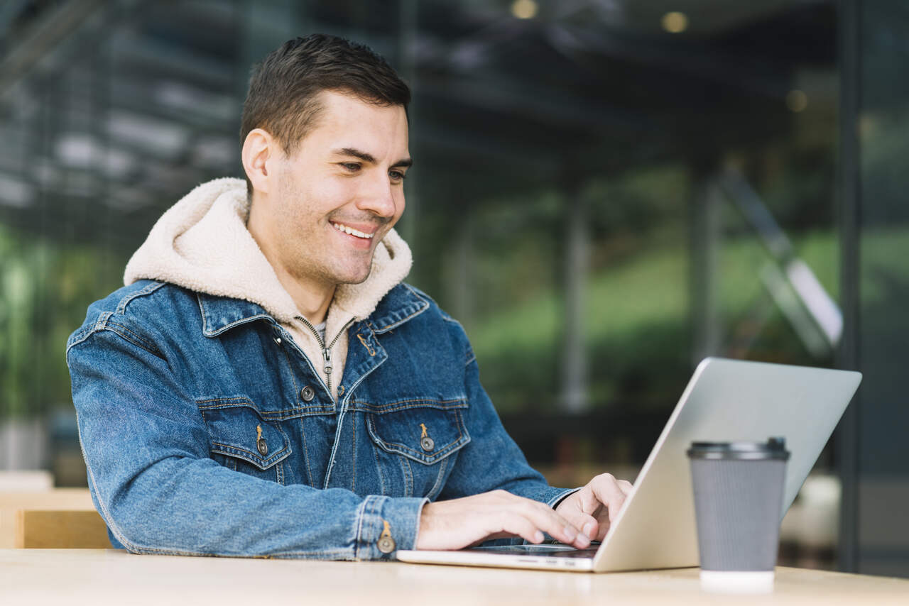 Jovem sorri enquanto está mexendo em seu notebook