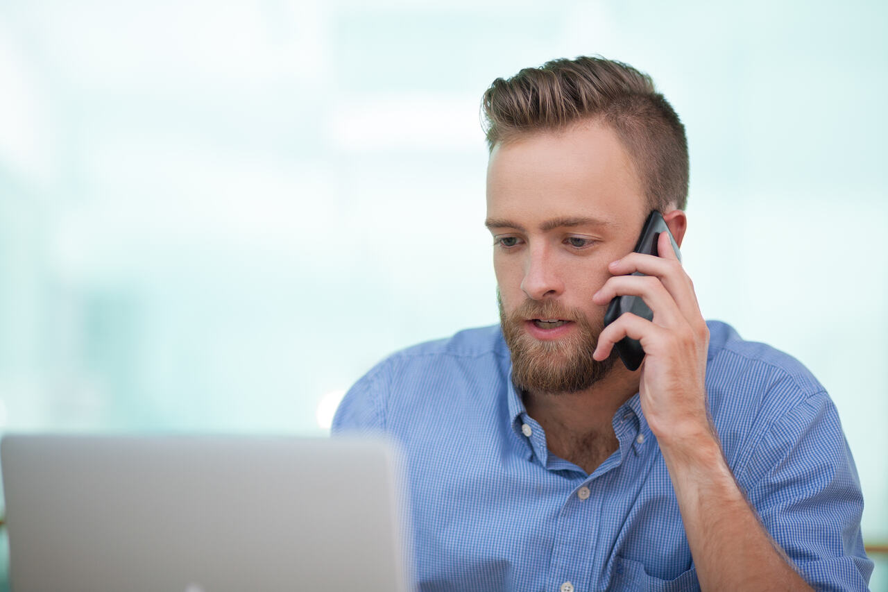 Profissional do setor administrativo verifica seu notebook enquanto atende cliente no telefone