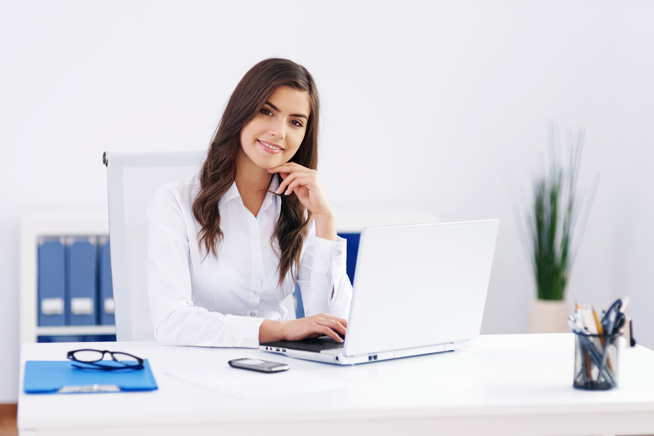 Assistente Administrativo posa sorridente enquanto trabalha em sua mesa 