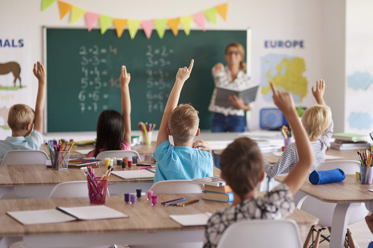 Alunos levantam a mão para responder pergunta da professora 