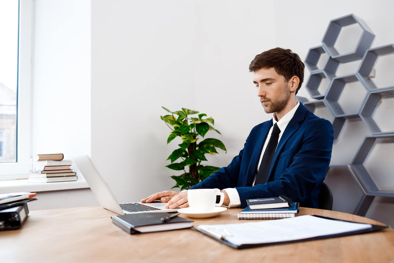 Homem trabalha em seu notebook sentado em sua mesa 