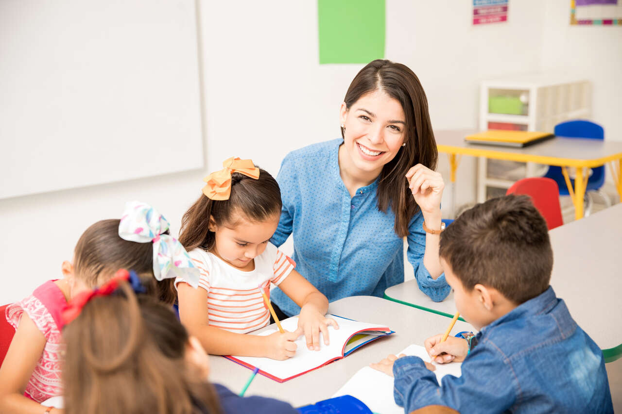 Professora de Educação Infantil posa enquanto faz atividades com alunos 